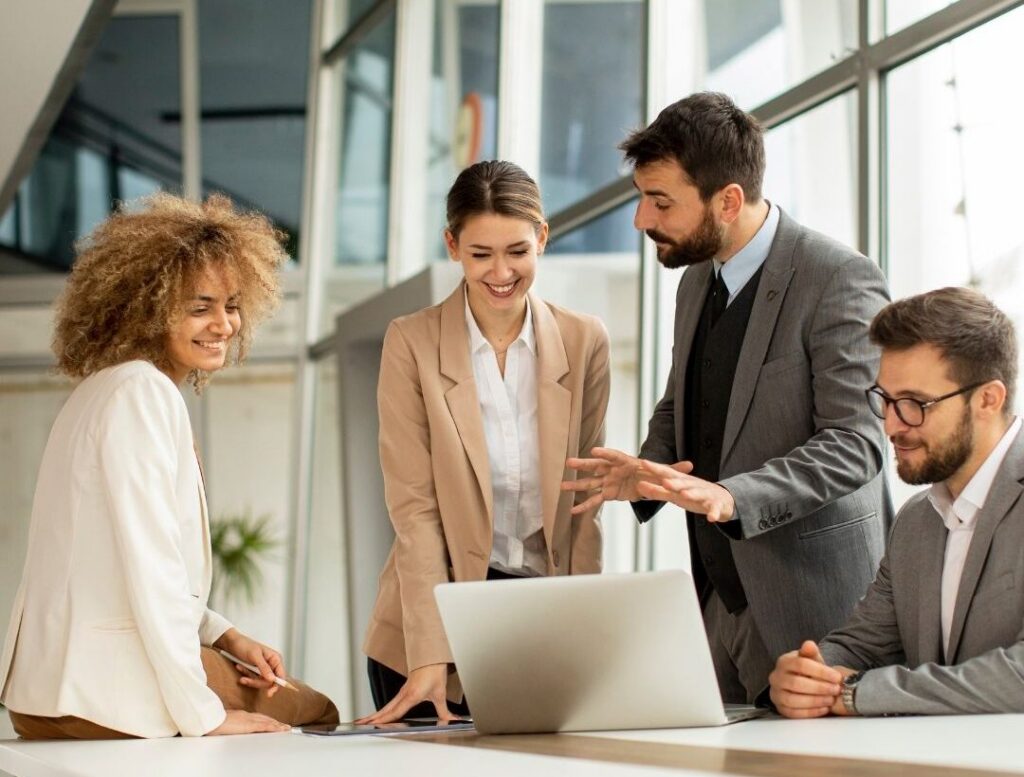 Vier Personen arbeiten gemeinsam an einem Laptop an einem Tisch in einem hellen Büro.