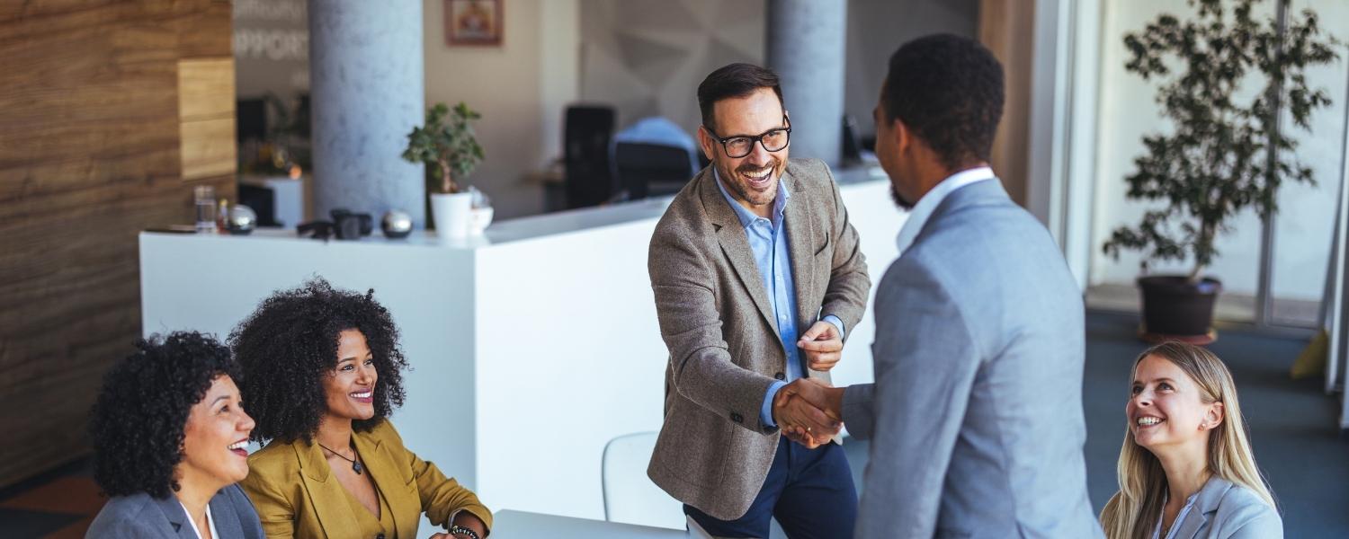 Mehrere berufstätige Personen sitzen in einem Meetingraum zusammen, tragen Business-Casual-Outfits und führen ein freundliches Gespräch.