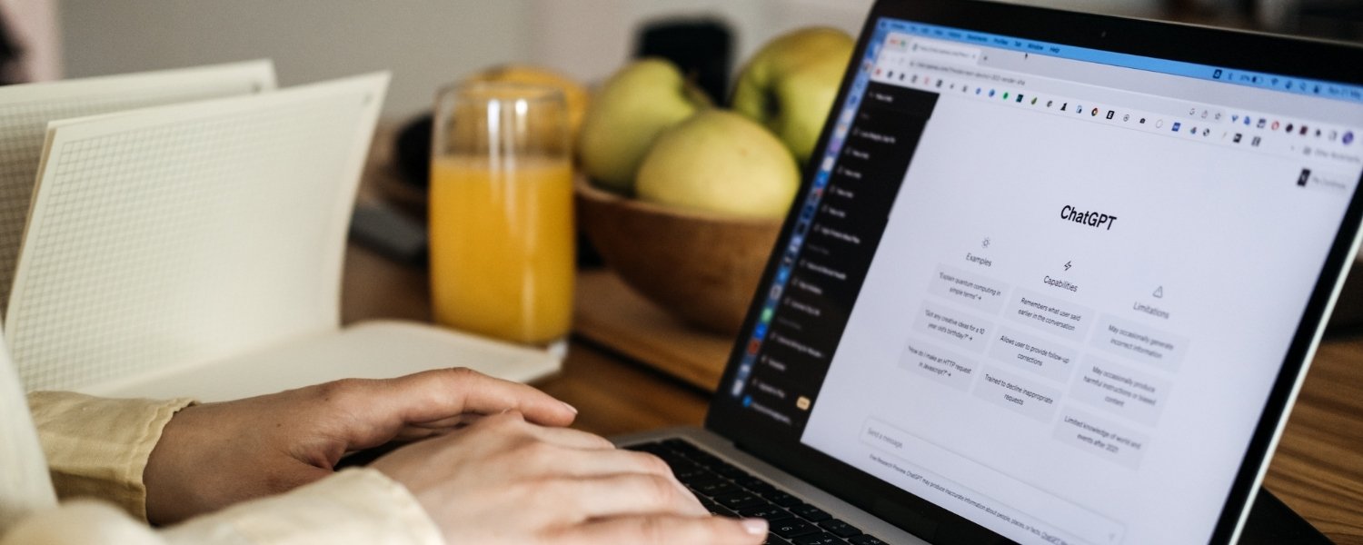 Person tippt an einem Laptop mit geöffneter ChatGPT-Oberfläche auf dem Bildschirm, auf dem Schreibtisch stehen ein Glas Orangensaft und eine Schale mit Äpfeln.