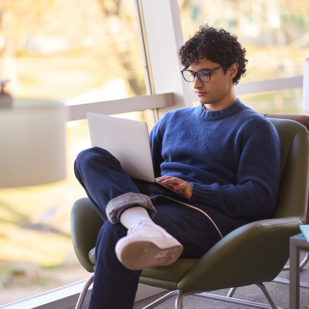 Junger Mann sitzt in modern eingerichtetem Raum und arbeitet am Laptop.