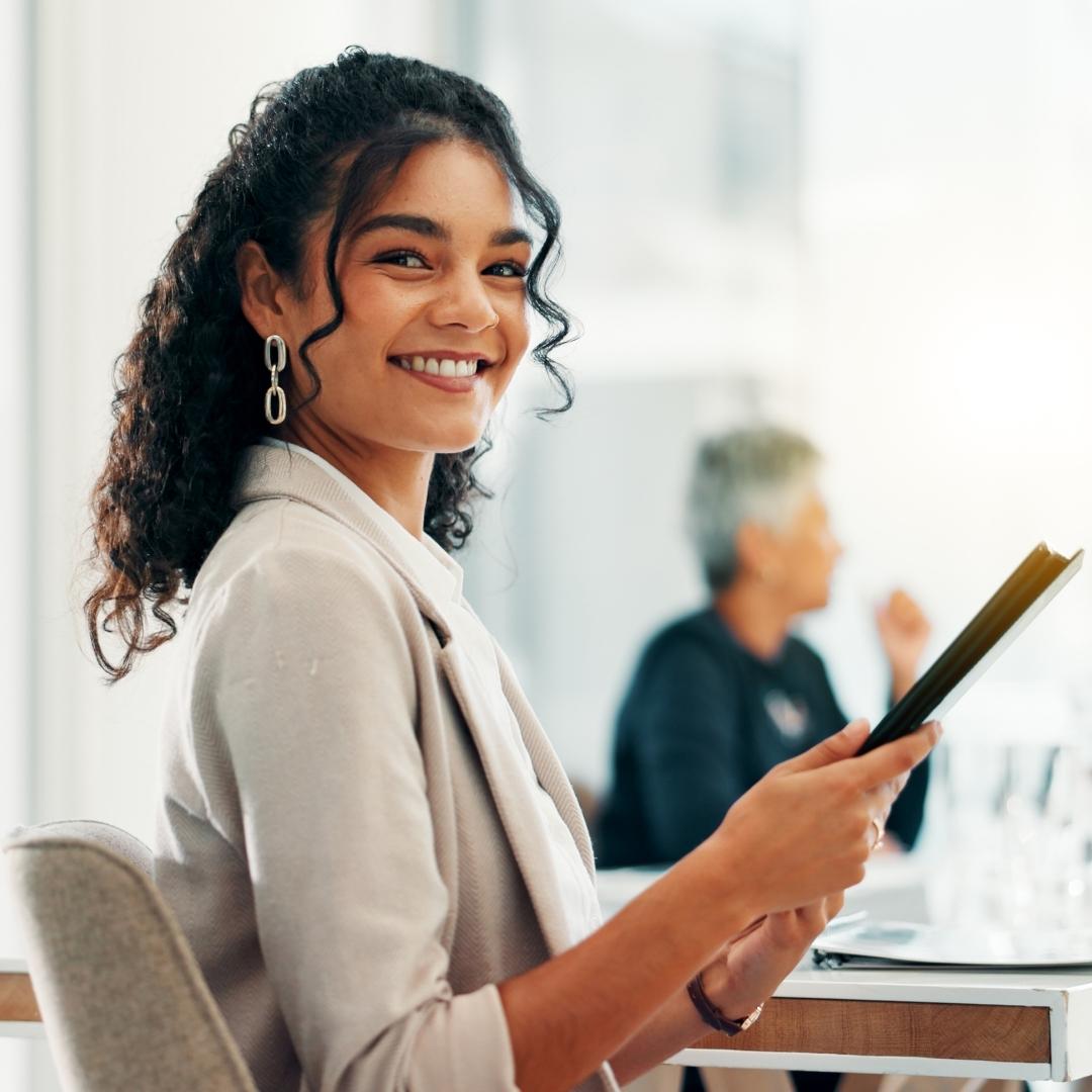 Eine junge Frau lächelt in die Kamera und hält eine Bewerbungsmappe in der Hand.