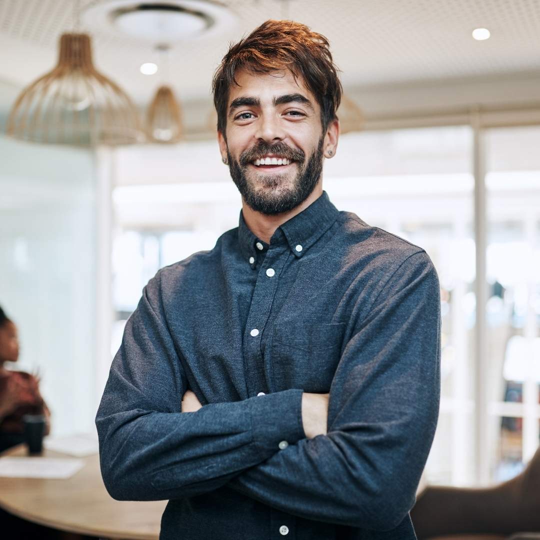 Mitarbeiter steht mit verschränkten Armen lächelnd im Büro – Symbolbild für Führung, klare Kommunikation und Top-Down-Kommunikation im Unternehmen.