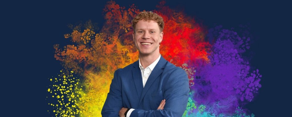 Portrait eines Deloitte Consultants vor farbigem Pride-Hintergrund in Regenbogenfarben. Niclas trägt einen blauen Anzug und lächelt in die Kamera.