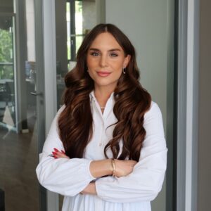 Porträt von Amelie Elisabeth Hornstein, Key Account & Partnerships Managerin bei SQUEAKER. Sie trägt eine weiße Bluse, steht mit verschränkten Armen in einem modernen Büro mit Glaswänden und blickt in die Kamera.
