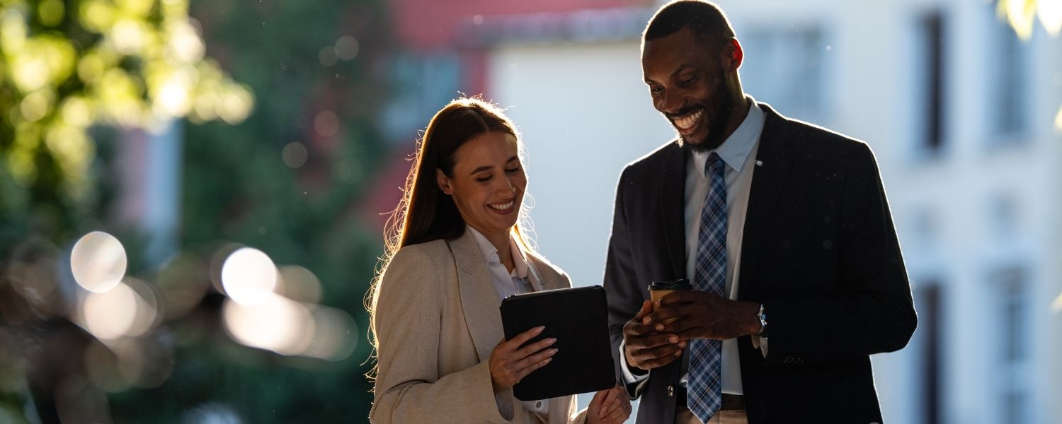 Zwei junge Professionals im Business-Outfit schauen lächelnd auf ein Tablet – symbolisch für den Karriereeinstieg ins Consulting durch eine Spring Week.